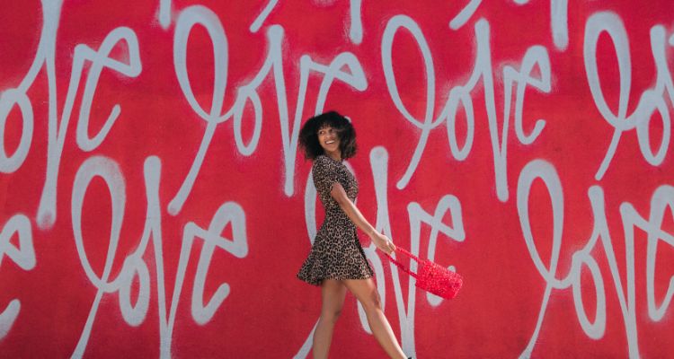 Woman posing in front of red wall with love written in white several times.